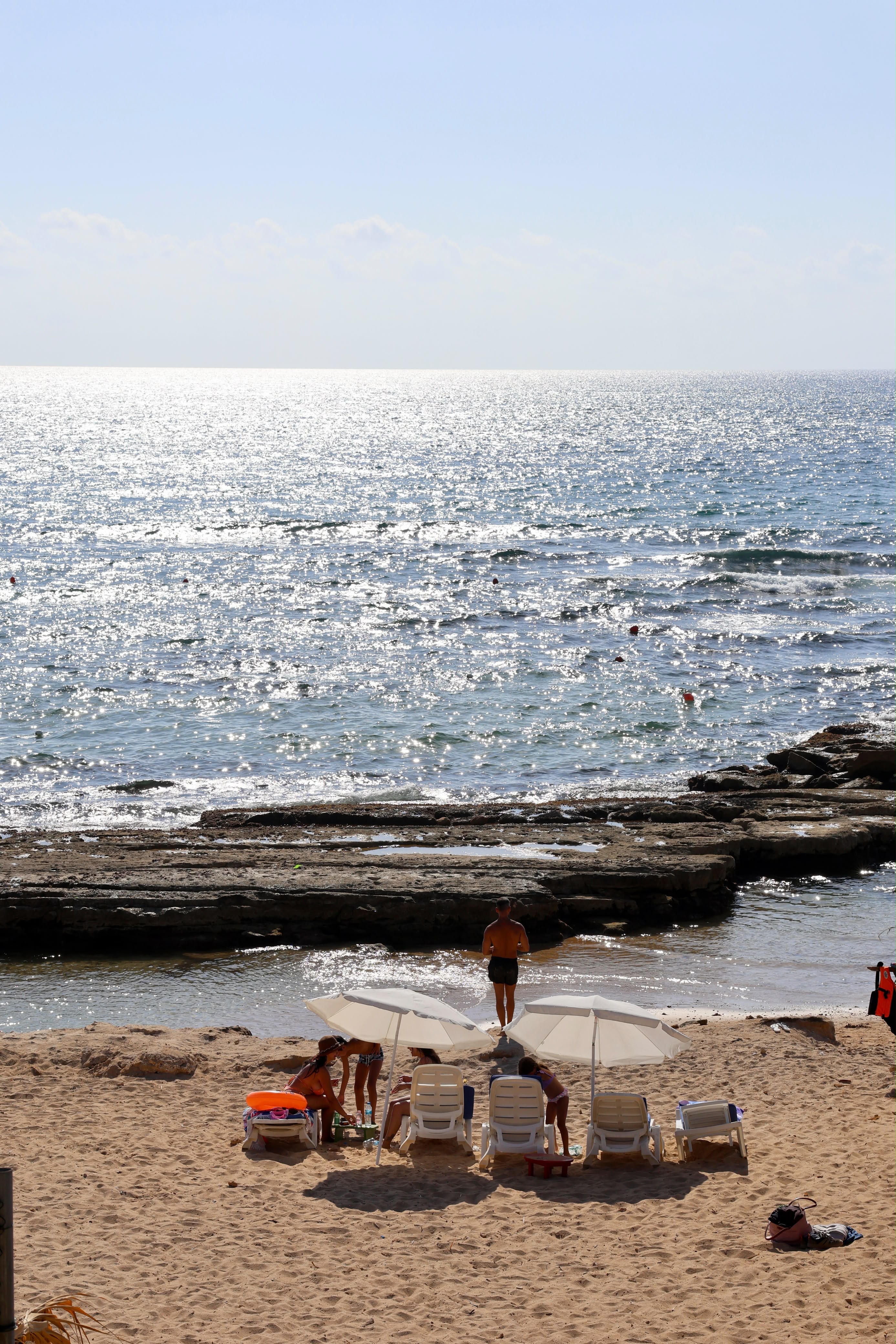 Guests relaxing on sun loungers by the rocky shore at Side B